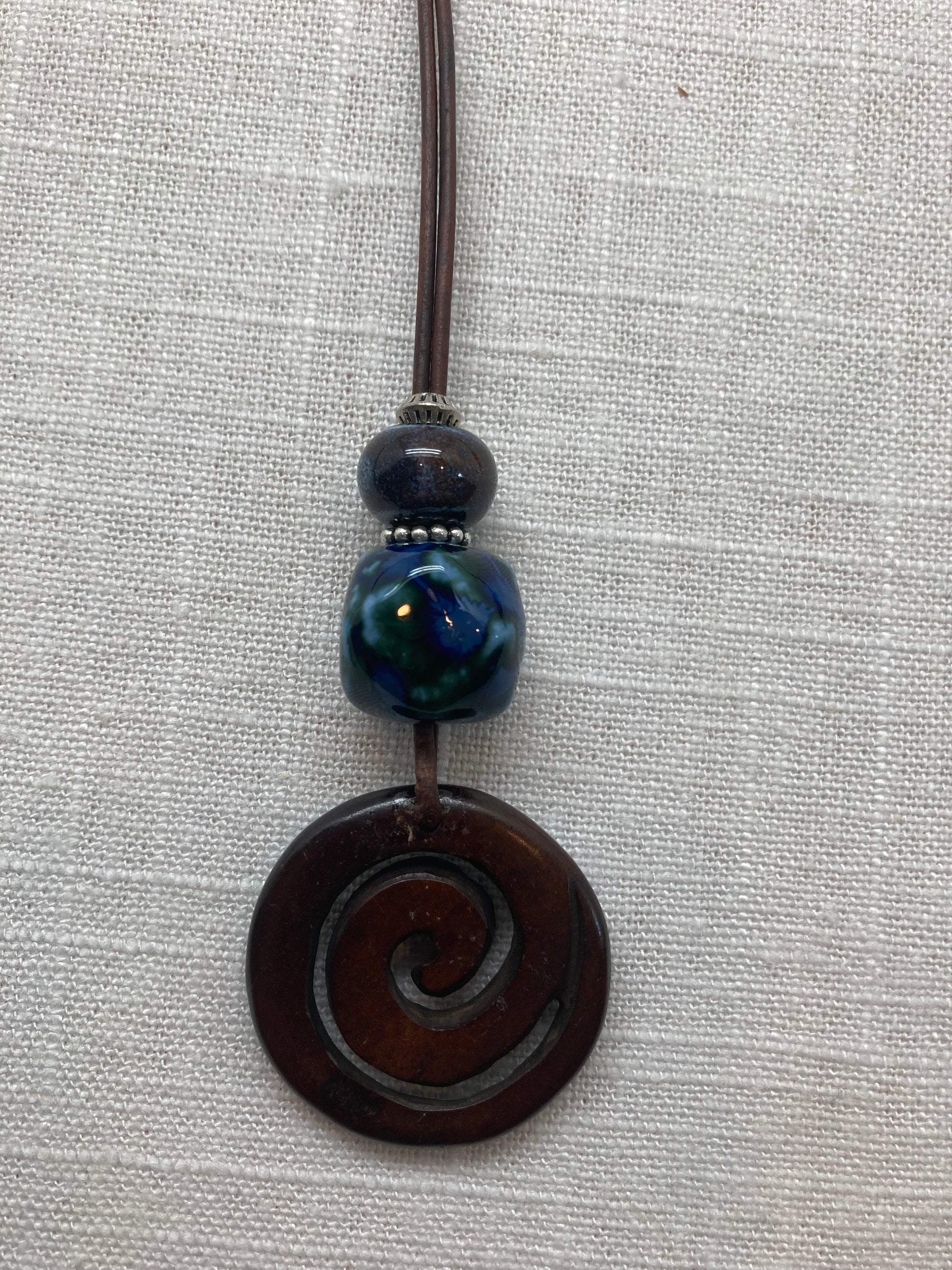 dark brown leather necklace with dark blue beads and dark carved spiral wood pendant
