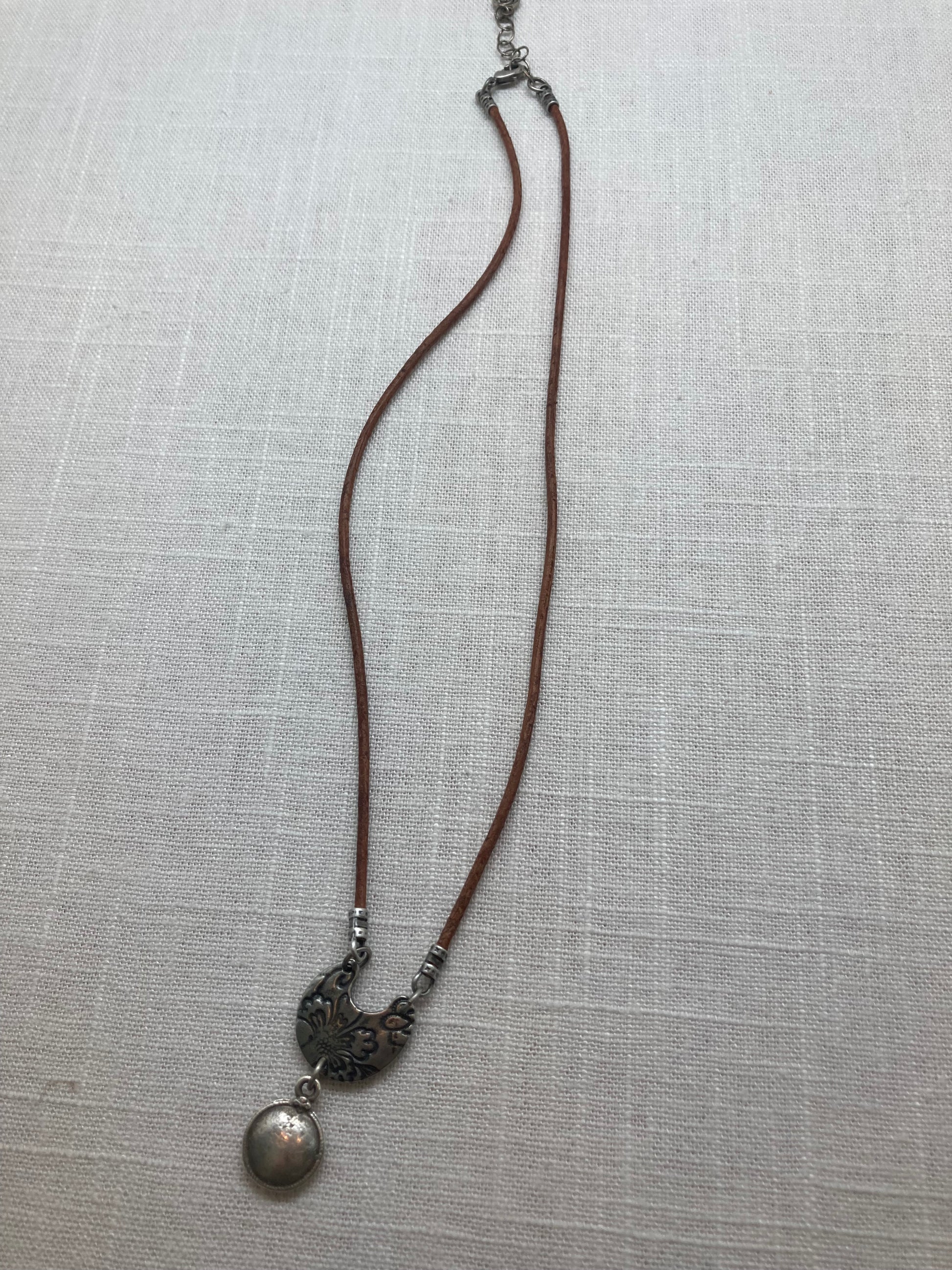 rustic brown leather necklace with half-moon charm attached to a circular charm